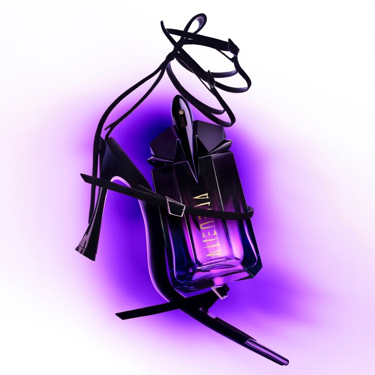 A sleek purple perfume bottle is elegantly draped with black strappy high heels, set against a bright white background with a subtle purple gradient.