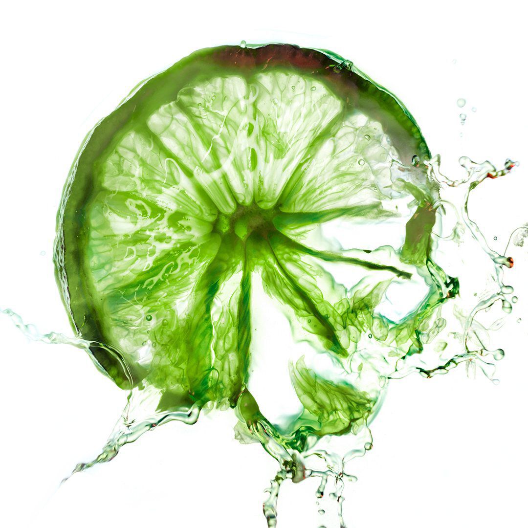 A close-up of a sliced lime, glistening with droplets of water and illuminated by soft, diffused light, showcasing its vibrant green color and textured rind.