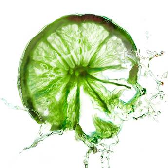 A close-up of a sliced lime, glistening with droplets of water and illuminated by soft, diffused light, showcasing its vibrant green color and textured rind.