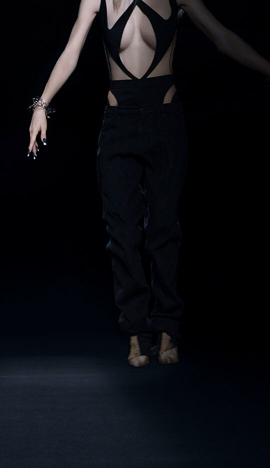 A person is wearing a stylish, revealing outfit with cut-out details, and is depicted mid-jump against a dark background, emphasizing their silhouette.