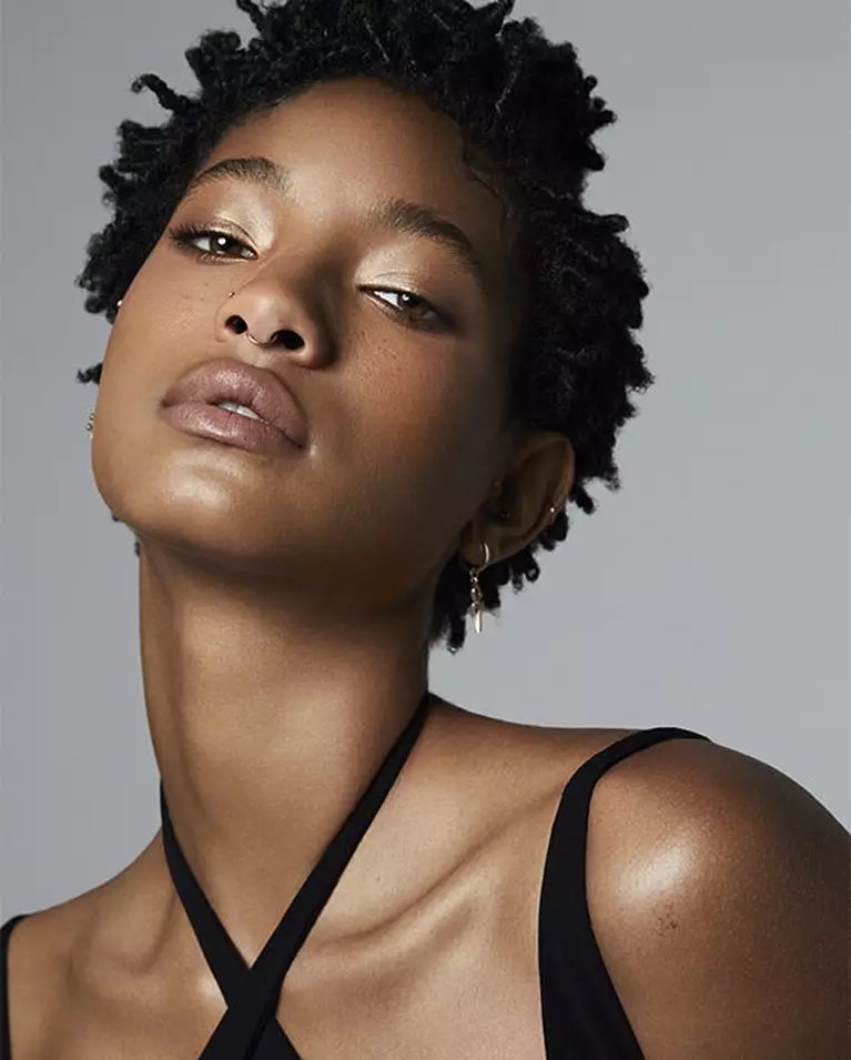 A close-up portrait of a young woman with textured hair, wearing a black top, exuding confidence and grace.
