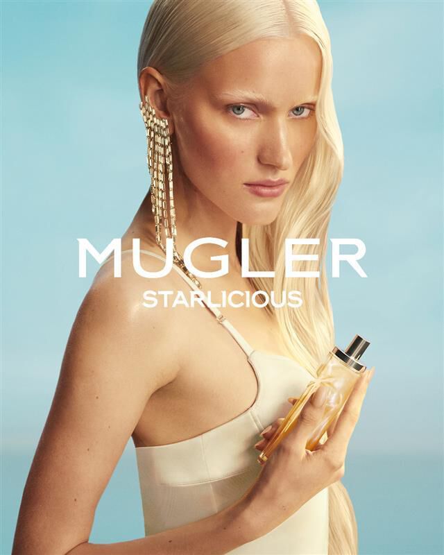 Mugler Starlicious Les Eaux Gourmandes campaign banner with model in pale yellow dress holding Pineapple Musk bottle against a soft blue sky.