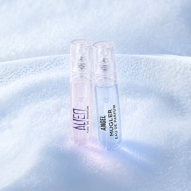 two mugler samples standing elegantly on a bed of pristine, sparkling white snow under soft blue light.