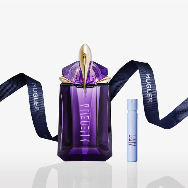 A purple perfume bottle with a gold accent, accompanied by a small spray vial, set against a white background. The bottle features a decorative ribbon labeled "MUGLER."