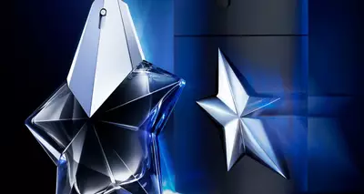 Alt text: A stylish fragrance bottle designed in the shape of a star, with a sleek black container in the background, both set against a dark backdrop with blue lighting accents.