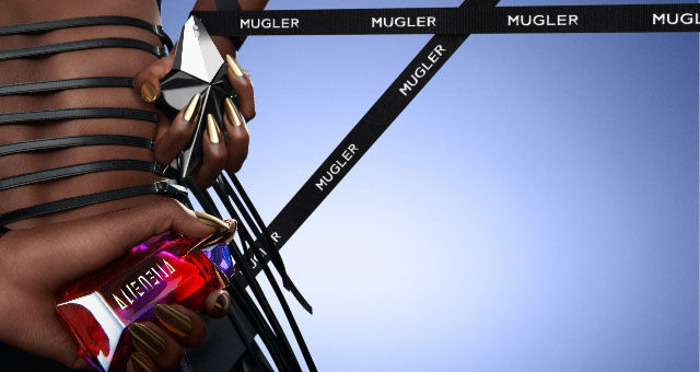 A close-up of a person's hand holding two colorful perfume bottles, adorned with long, pointed nails, against a soft gradient background. A black ribbon with "Mugler" is also visible.