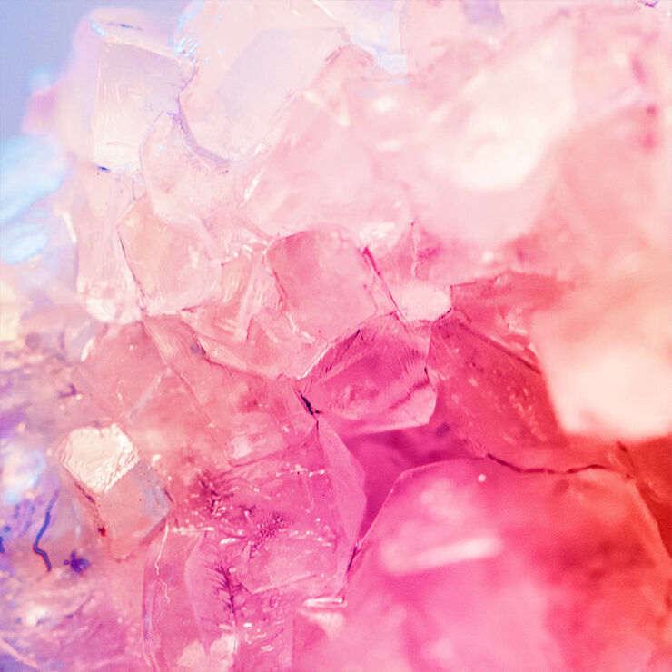 Close-up of a cluster of translucent pink crystals with sharp edges, reflecting light in various shades.