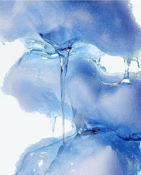 Close-up of melting textured blue ice with clear liquid dripping down against a white background.