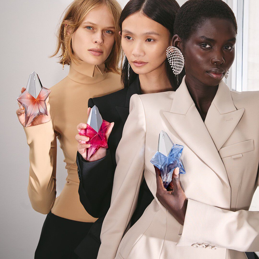 A crop of three models holding Mugler's iconic star-shaped perfume bottles in peach, vibrant pink, and light blue.