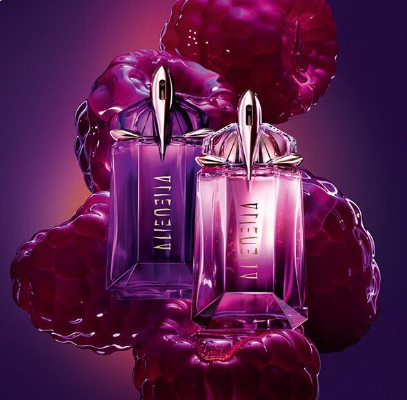 Two purple and pink Alien Hypersense perfume bottles by Mugler, surrounded by large, glossy purple raspberries against a dark background.