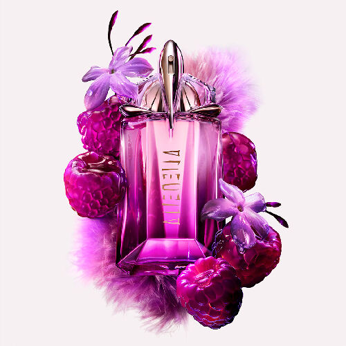 A purple, geometric glass perfume bottle surrounded by purple raspberries and delicate flowers.
