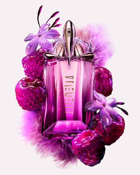 A purple, geometric glass perfume bottle surrounded by purple raspberries and delicate flowers.