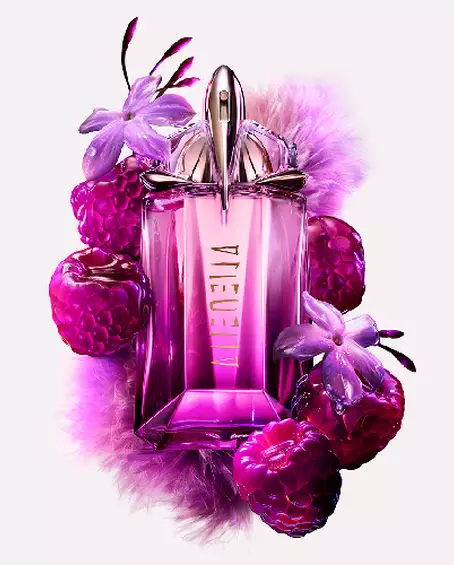 A purple, geometric glass perfume bottle surrounded by purple raspberries and delicate flowers.