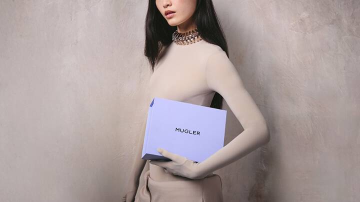 Model in beige bodysuit holding a light purple Mugler box.