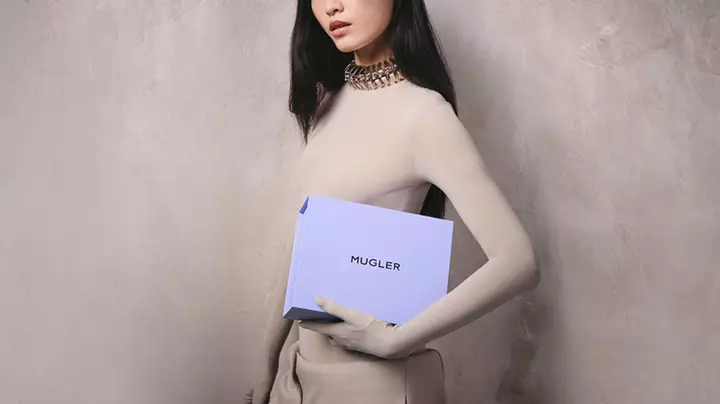 Model in beige bodysuit holding a light purple Mugler box.