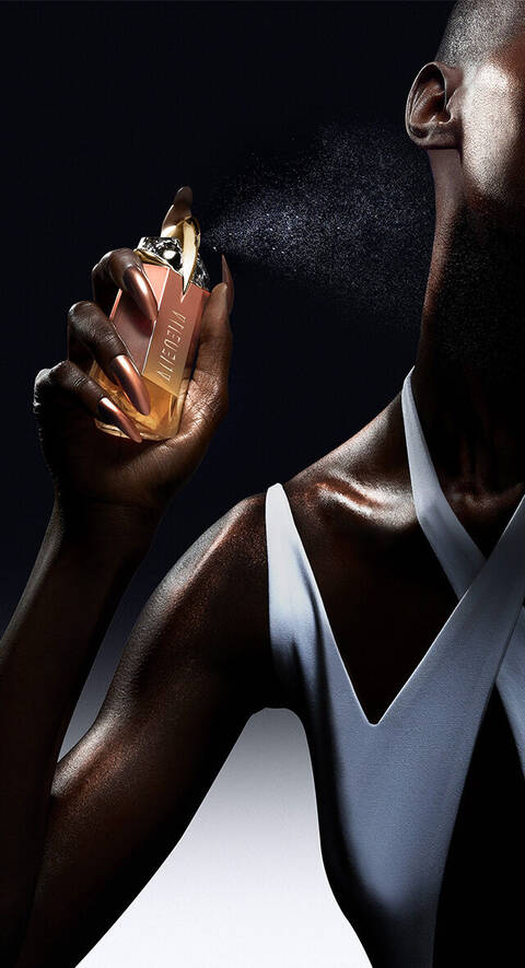 A close-up of a hand holding a stylish perfume bottle, spraying a fine mist against a dark background. The bottle features a sleek design with a luxury aesthetic.