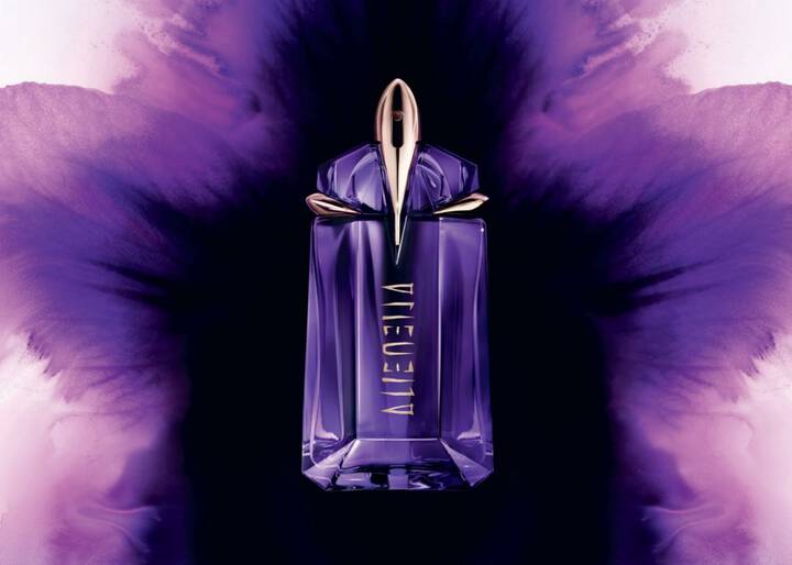 A futuristic purple and gold Mugler Alien perfume bottle displayed against an artistic watercolor-style purple flower bloom.