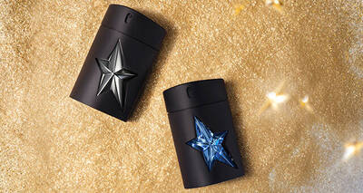 Two black perfume bottles, one with a silver star and one with a blue star, rest on a shimmering golden background.