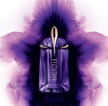A futuristic purple and gold Mugler Alien perfume bottle displayed against an artistic watercolor-style purple flower bloom.