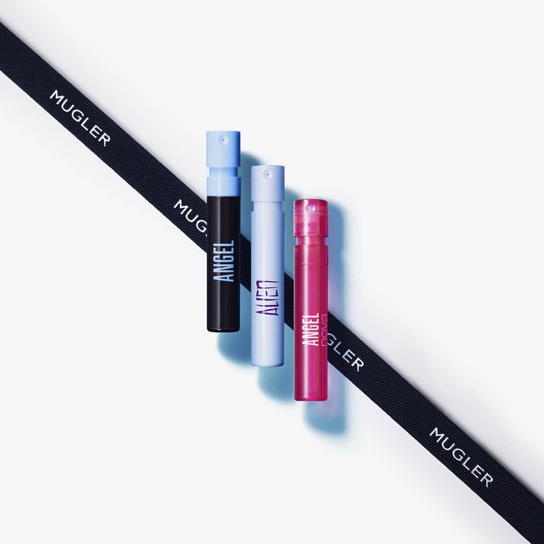 Three small fragrance spray bottles in black, blue, and pink, arranged next to a black ribbon labeled "MUGLER."