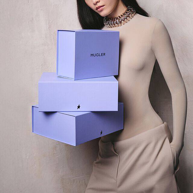 A woman holding a stack of three purple blue Mugler gift boxes with the star logo.