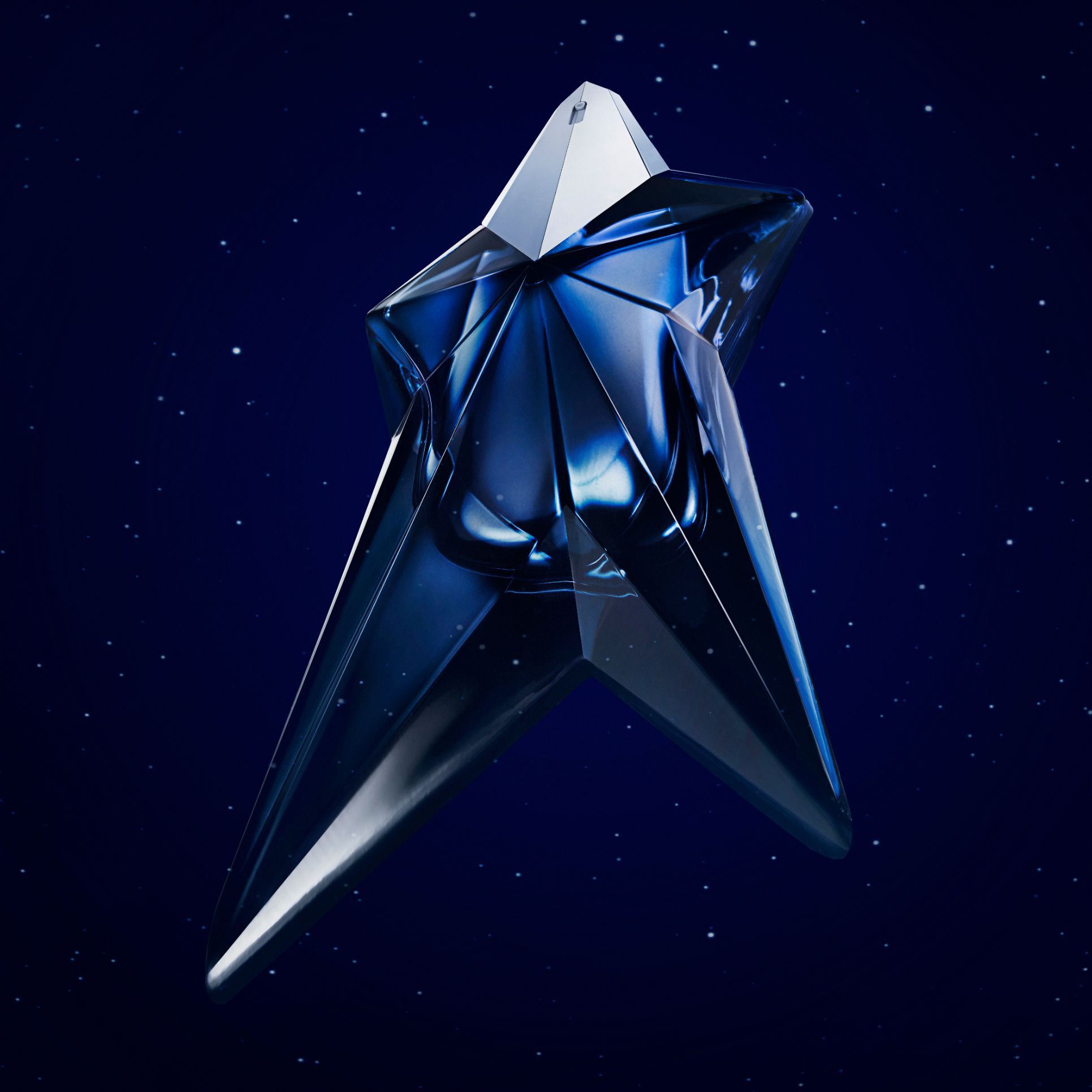 Alt text: A five-point star-shaped perfume bottle in a deep blue hue, set against a dark starry background, with text announcing the birth of a new fragrance from Mugler.