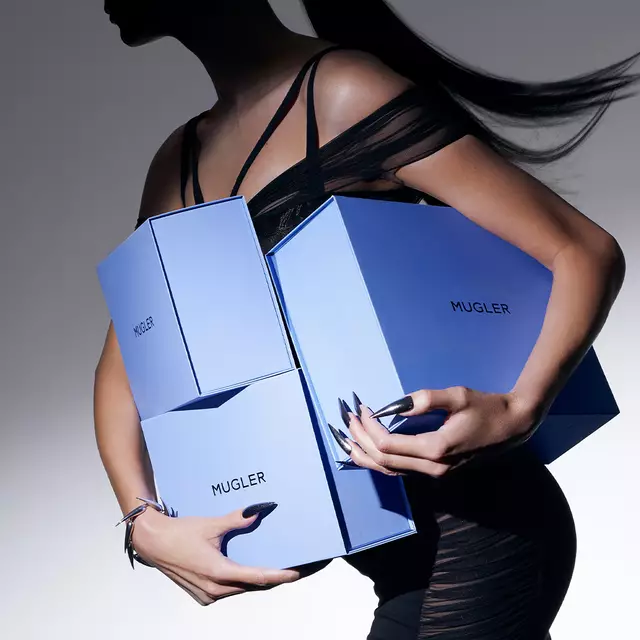 A silhouette of a person holding multiple blue boxes with the Mugler logo, wearing a black, elegant outfit.
