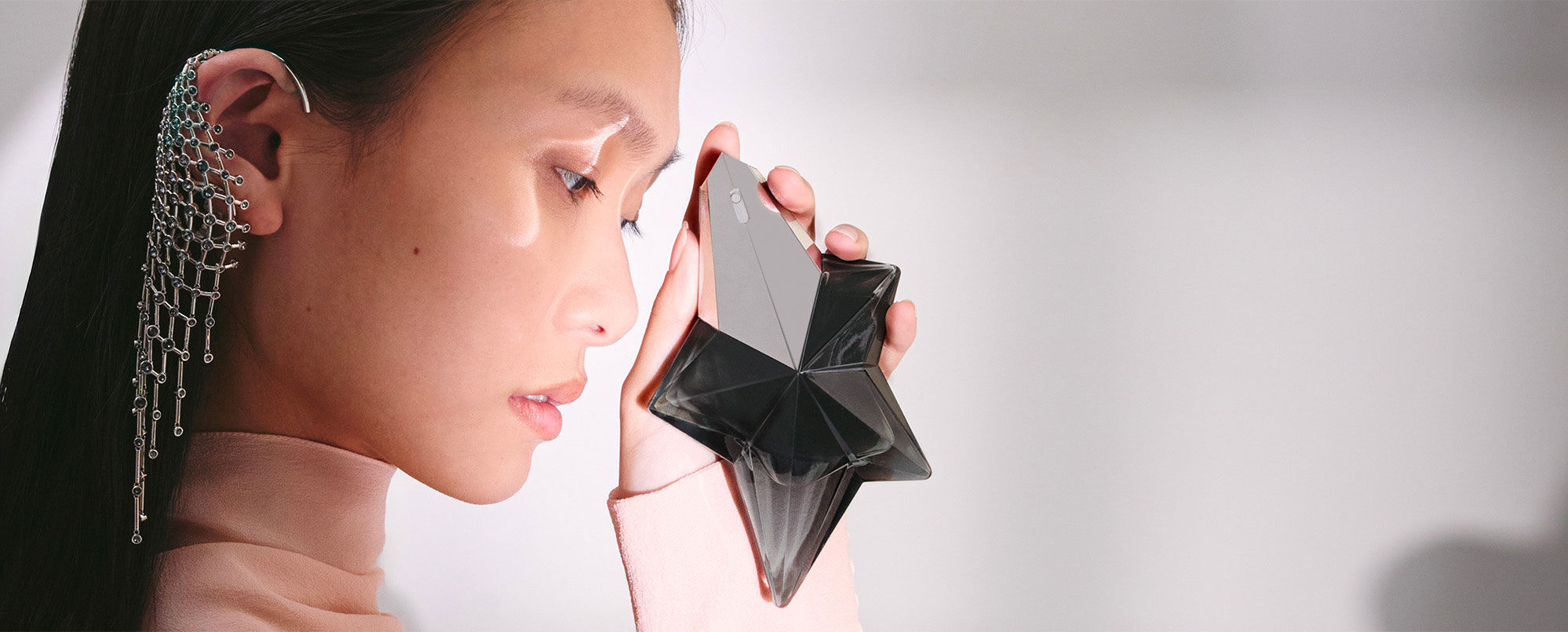 Woman applying Mugler Angel Fantasm star-shaped bottle behind her ear, sensual luxury fragrance lifestyle shot