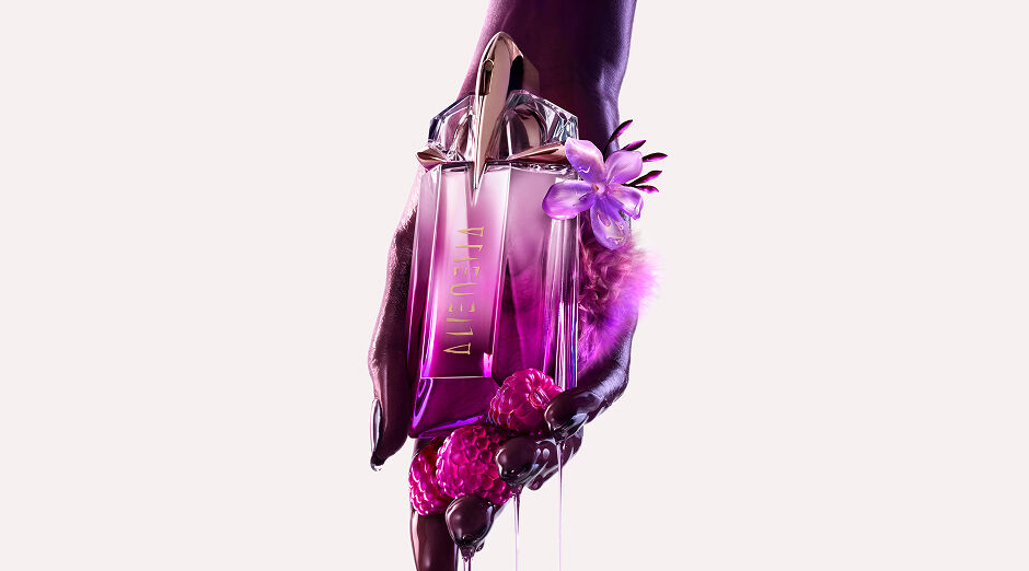  A hand gently holding the Mugler Alien Pulp bottle, with glistening pink berries and drips of liquid cascading from around it
