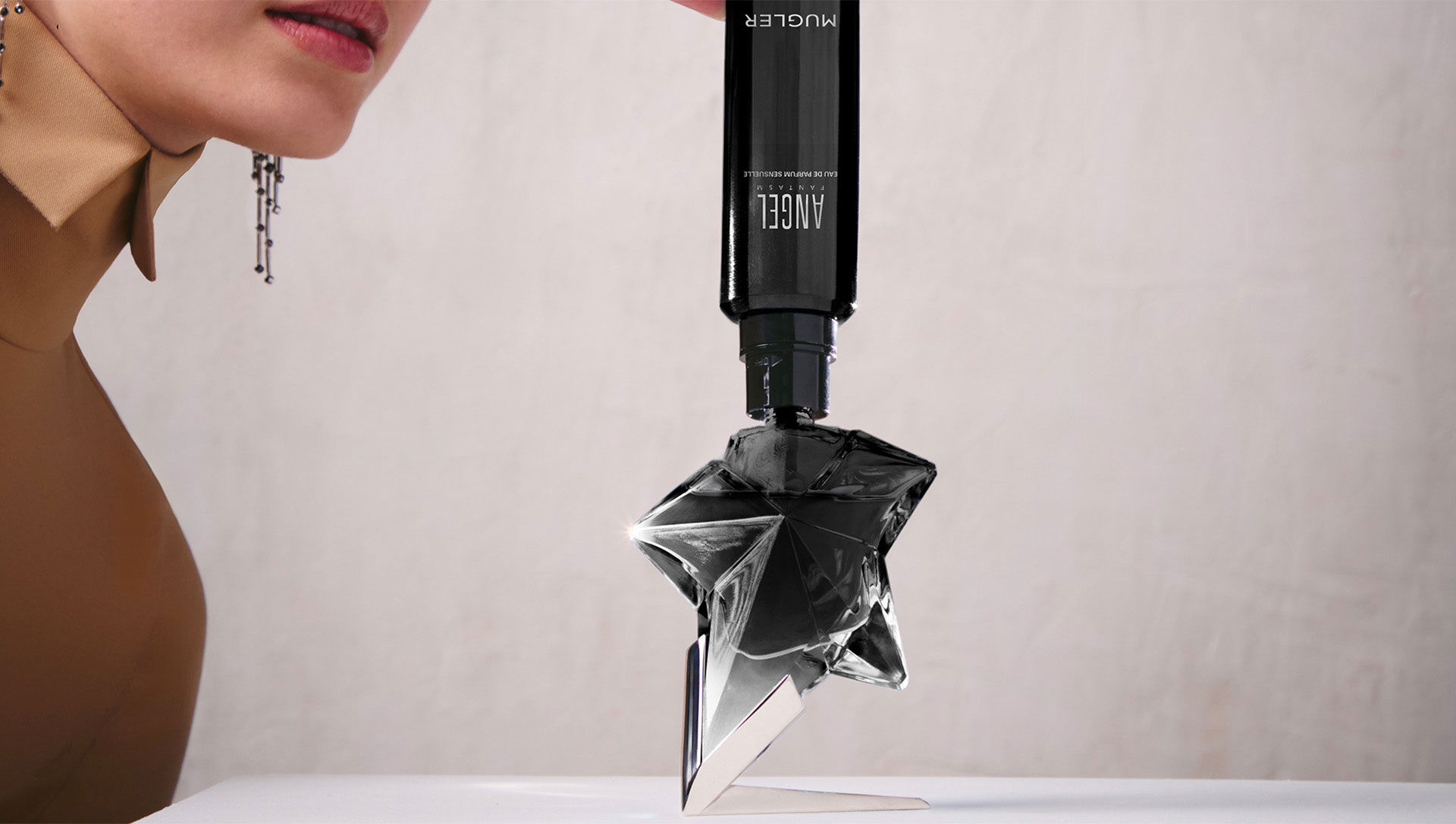 Woman using Mugler Angel Fantasm refill bottle to refill her star-shaped perfume bottle, eco-responsible refillable fragrance system