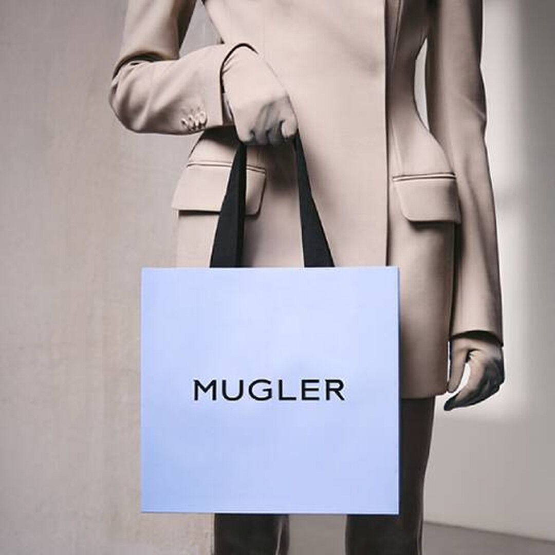 Person in a beige suit holding a pale blue Mugler shopping bag