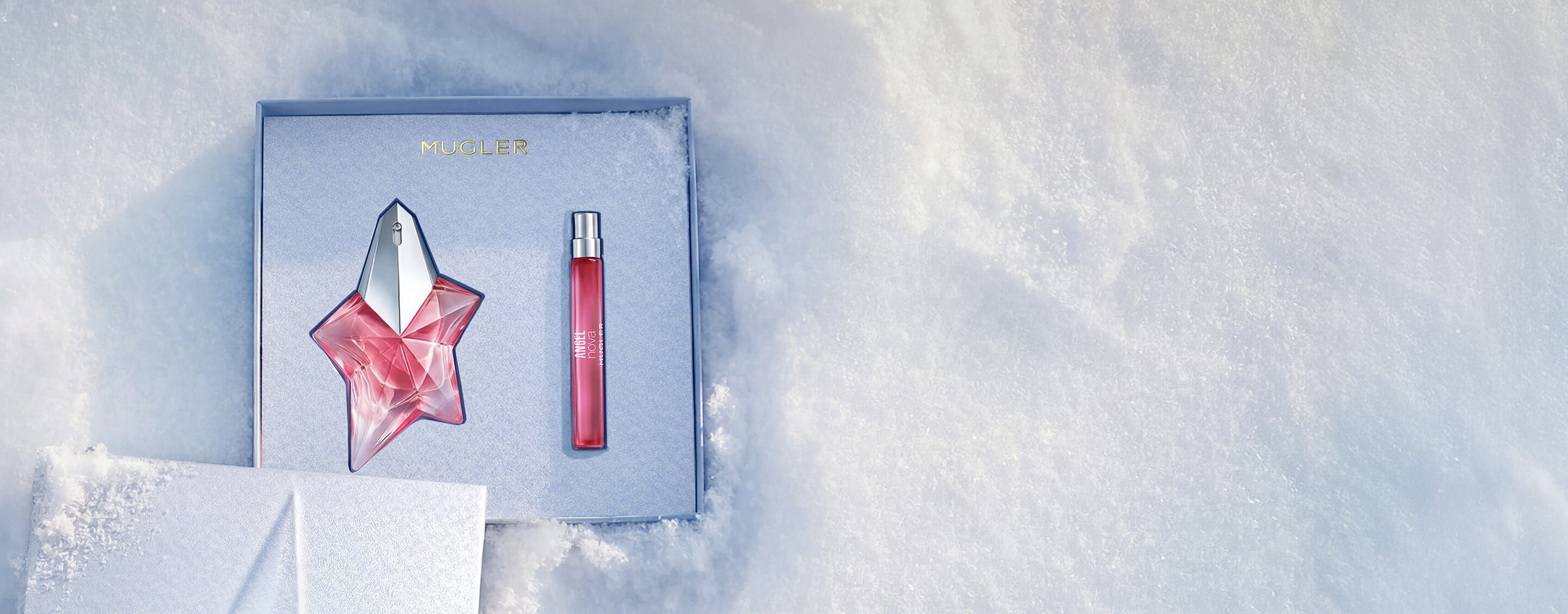 An open, textured ice-blue glistening Mugler gift set resting on snow, revealing an angel nova eau de parfum 50ml gift set. text reads 'offer a gift to remember this holiday season, with angel nova's decadent gourmand notes wrapped in a sprakling gift set'