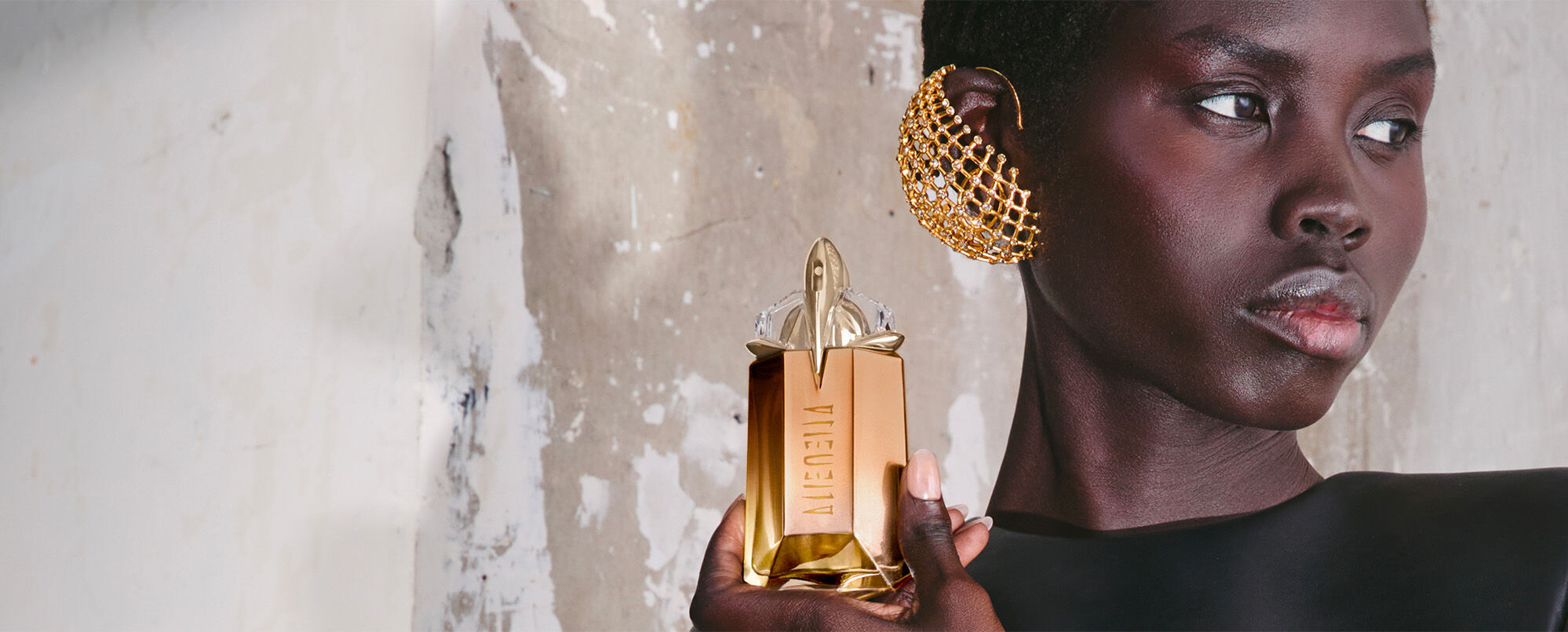 Elegant Black model holding Mugler Alien Goddess Supra Florale peach and gold talisman bottle, luxury fragrance campaign lifestyle shot