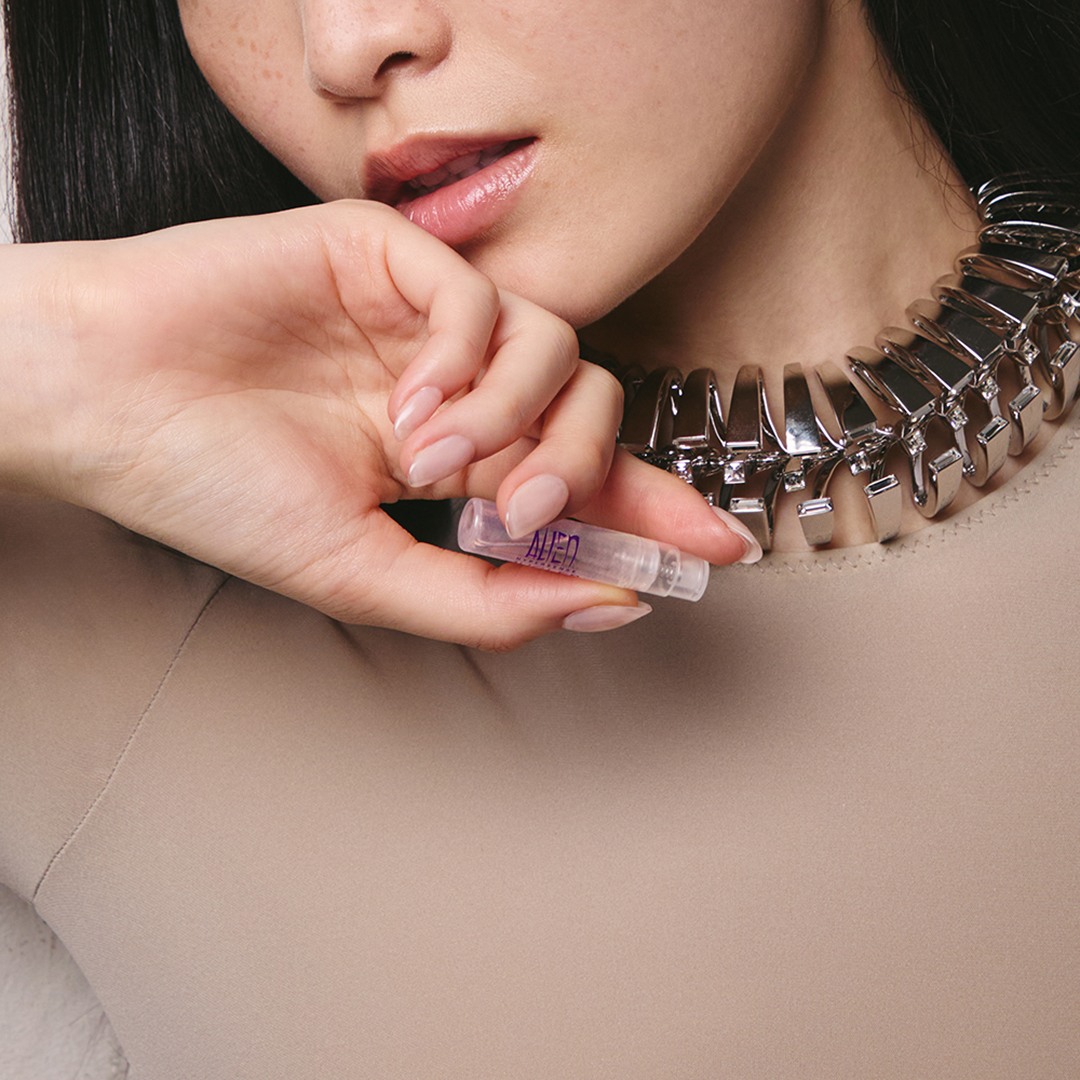 Hand holding an Angel Mugler perfume sample near a chunky silver necklace