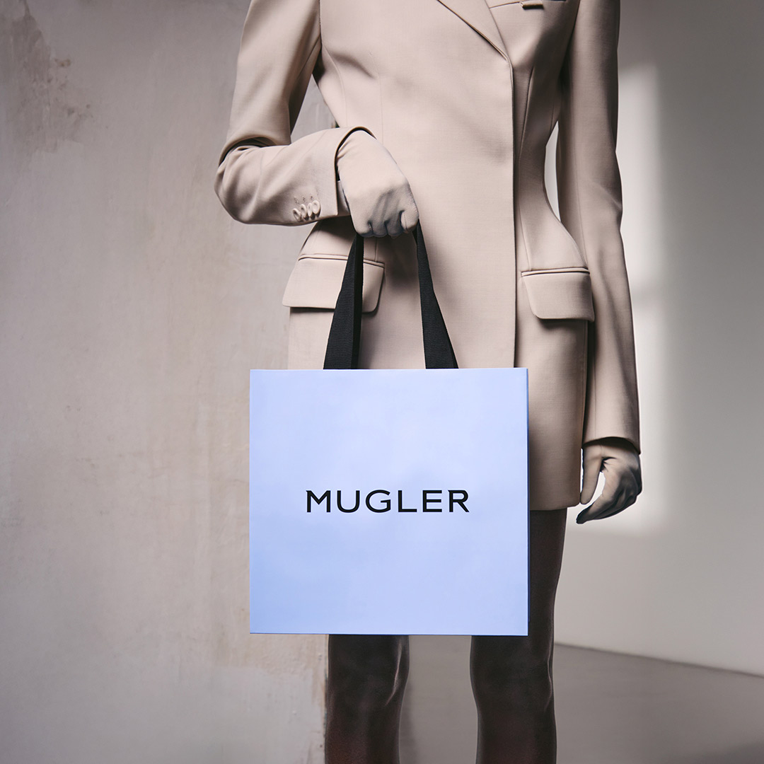 Person in a beige suit holding a pale blue Mugler shopping bag