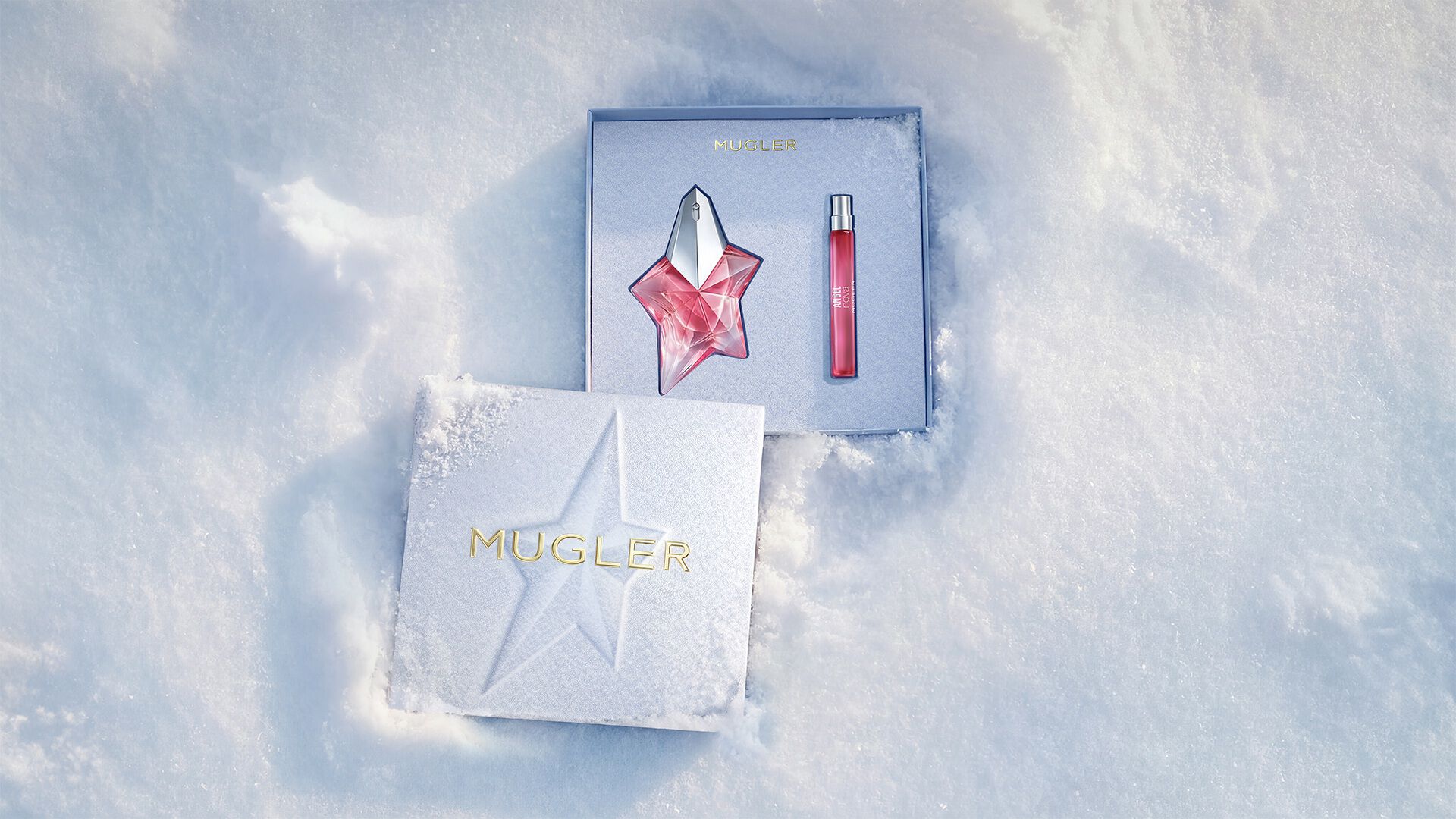 An open, textured ice-blue glistening Mugler gift set resting on snow, revealing an angel nova eau de parfum 50ml gift set