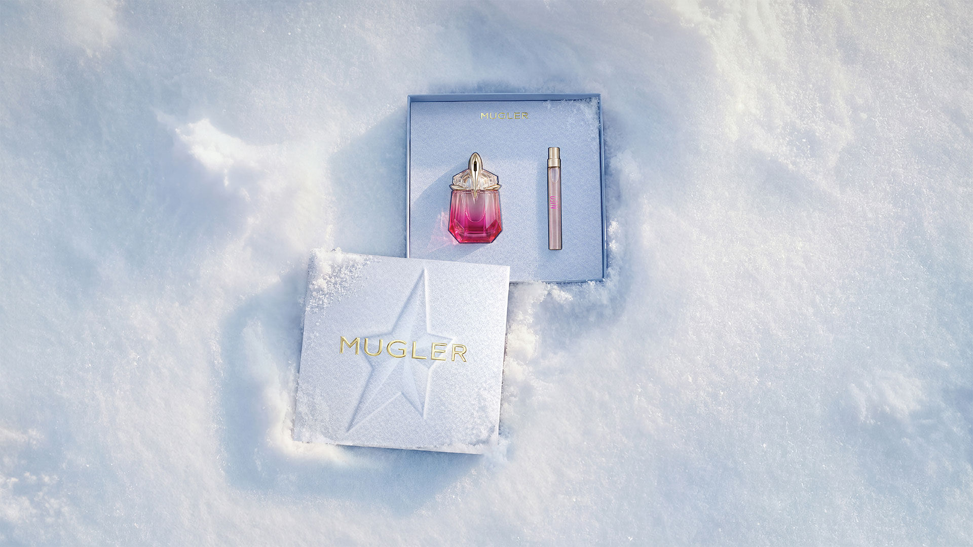 An open, textured ice-blue glistening Mugler gift set resting on snow, revealing an alien pulp eau de parfum 30 ml gift set. text reads "leave an unforgettable mark this holiday season with the fruity temptation of alien pulp wrapped in an elevated gift set