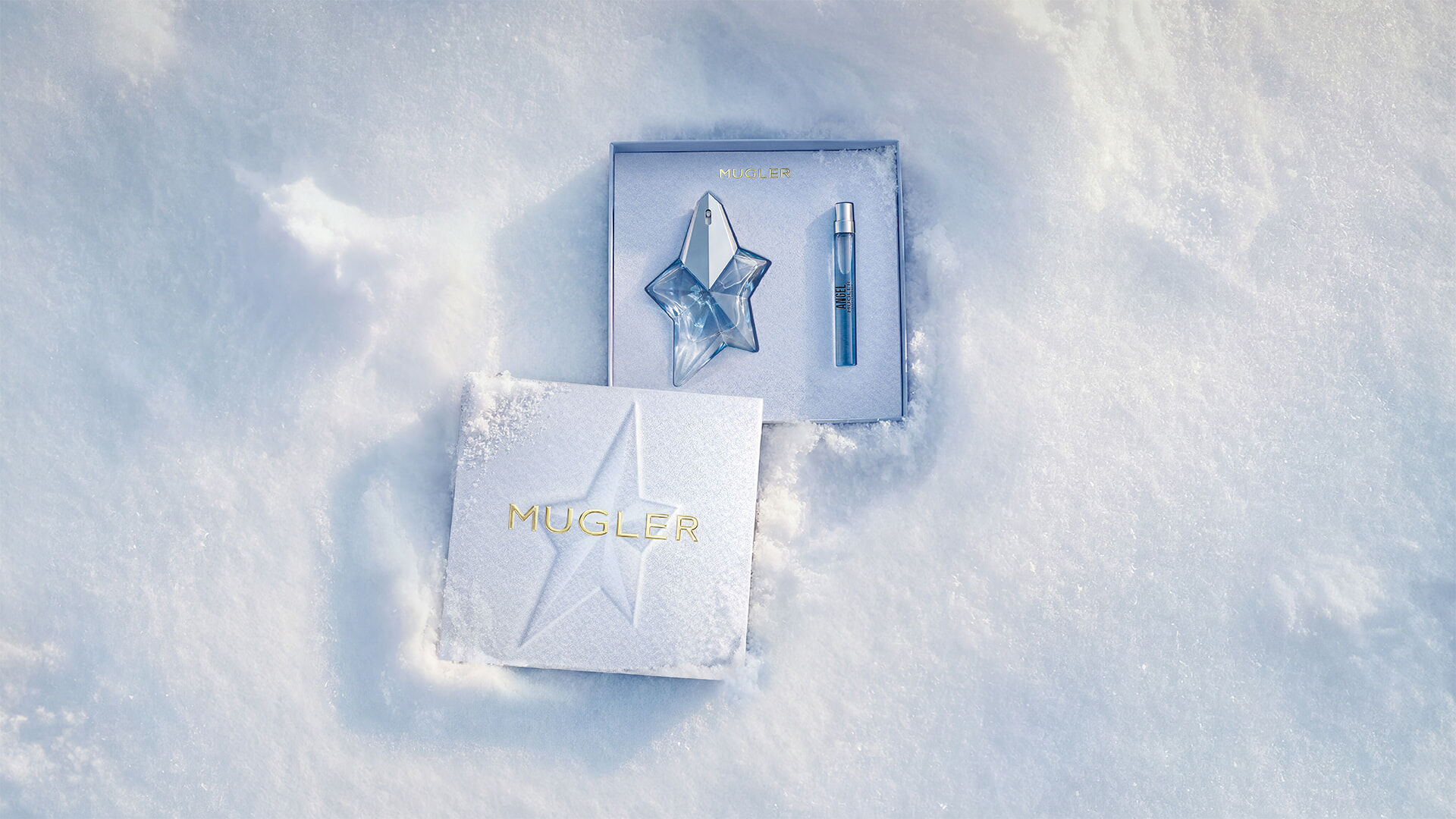 An open, textured ice-blue glistening Mugler gift set resting on snow, revealing an angel eau de parfum 25ml gift set