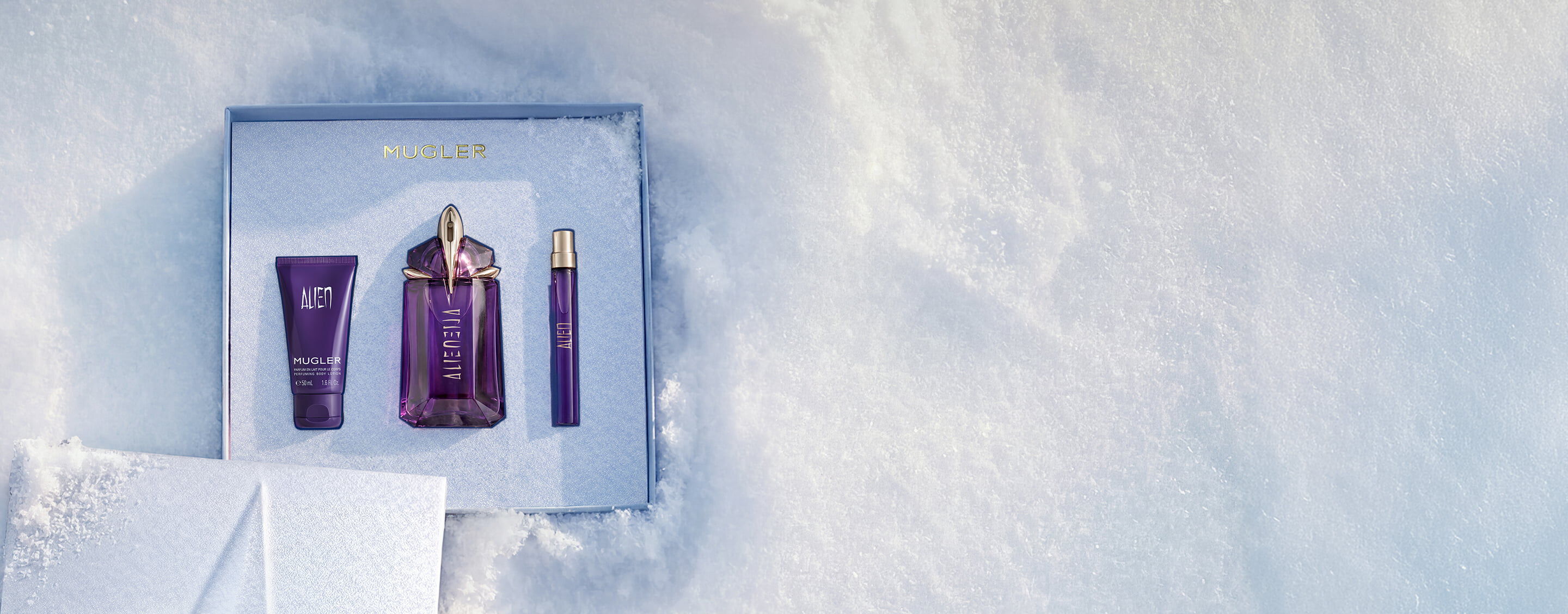 An open, textured ice-blue glistening Mugler gift set resting on snow, revealing an alien eau de parfum 60ml luxury gift set. text reads "offer a gift to remember this holiday season, with alien eau de parfum's powerful floral notes wrapped in a shiny gift set"