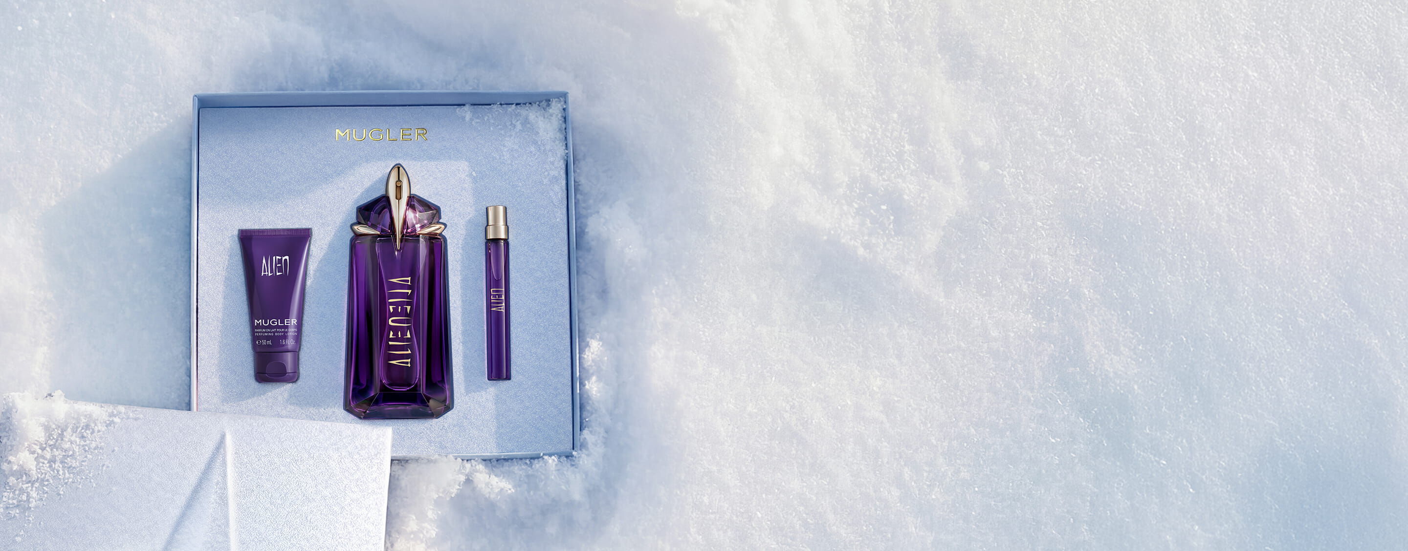 An open, textured ice-blue glistening Mugler gift set resting on snow, revealing an alien eau de parfum 60ml luxury gift set. text reads "offer a gift to remember this holiday season, with alien eau de parfum's powerful floral notes wrapped in a shiny gift set"