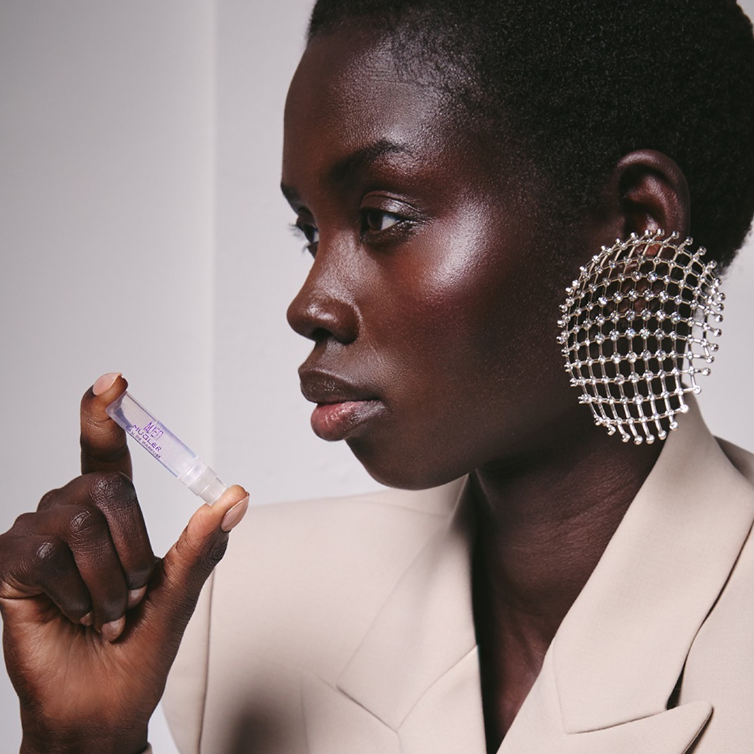 Person holding a small Angel Mugler perfume sample while wearing a large silver mesh earring