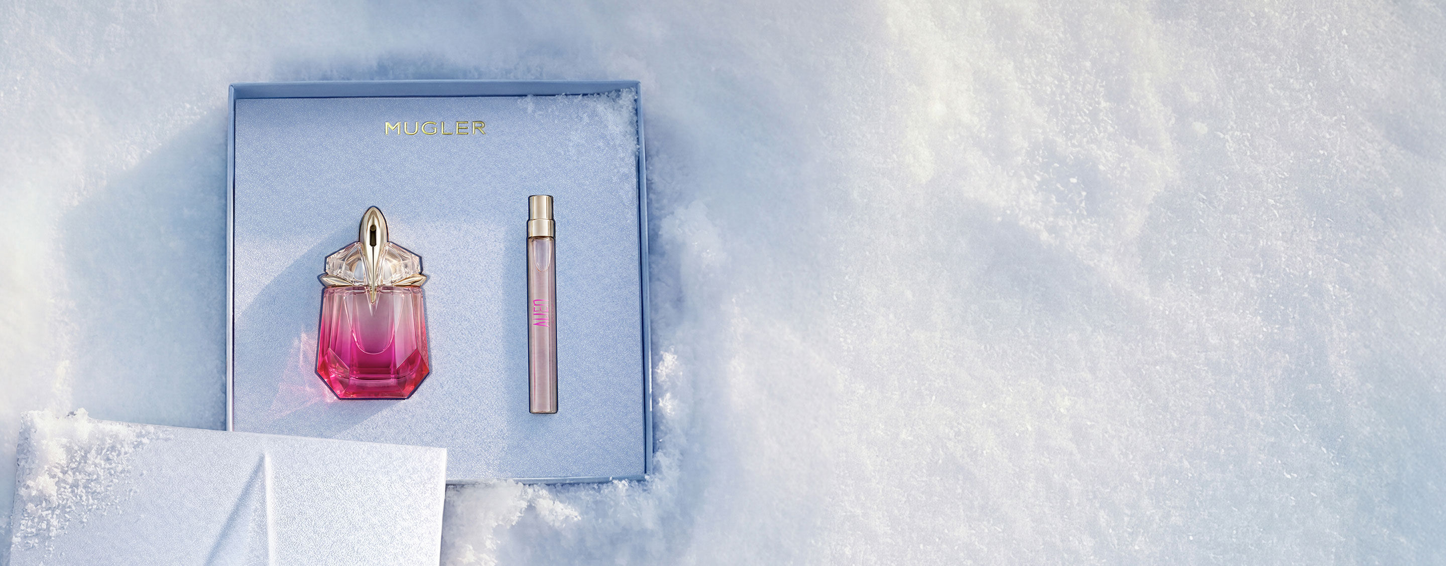 An open, textured ice-blue glistening Mugler gift set resting on snow, revealing an alien pulp eau de parfum 30 ml gift set. text reads "leave an unforgettable mark this holiday season with the fruity temptation of alien pulp wrapped in an elevated gift set