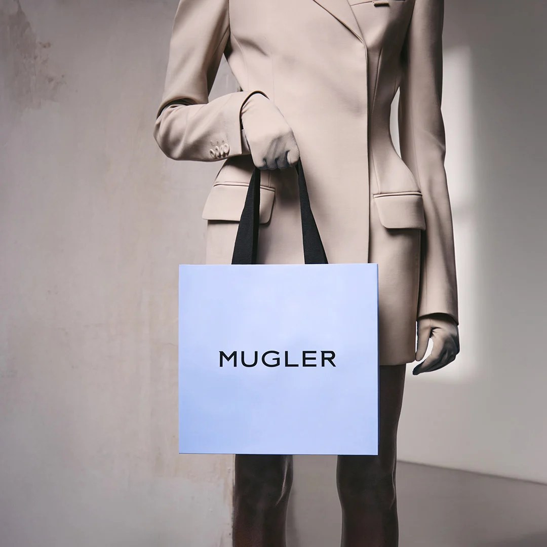 Person in a beige suit holding a pale blue Mugler shopping bag