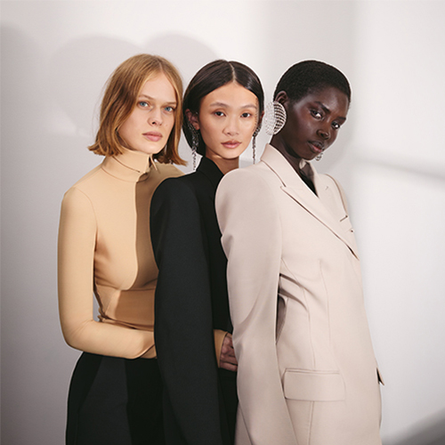 Three models posing in neutral and black tailored outfits.​