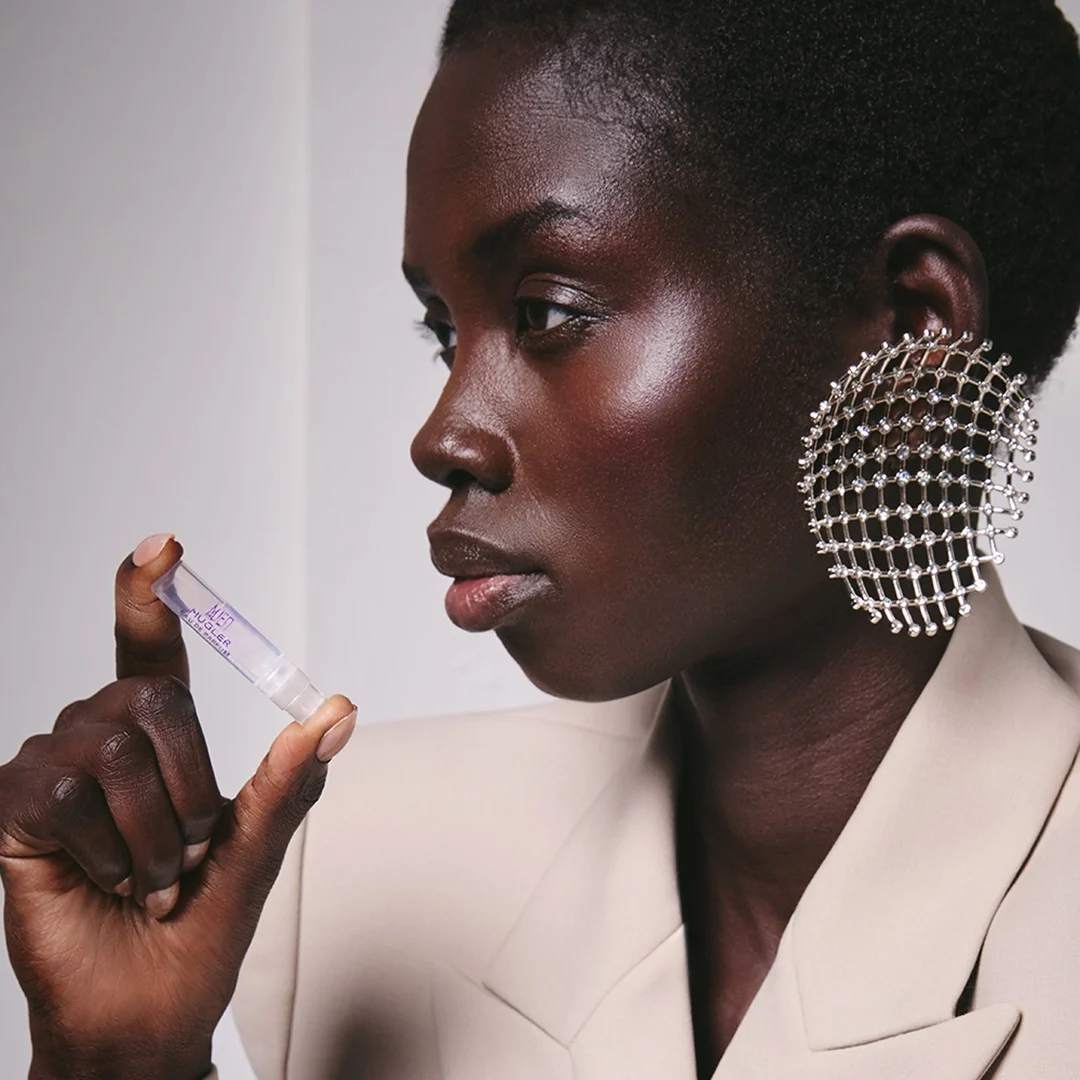 Person holding a small Angel Mugler perfume sample while wearing a large silver mesh earring