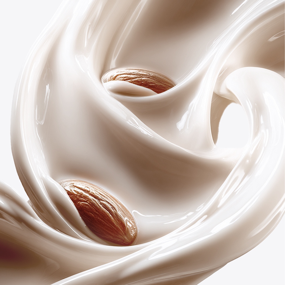 Two whole almonds swirling in a smooth, glossy splash of rich white cream.