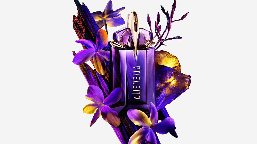 Promotional shot of Mugler's Alien Eau De Parfum in the midst of blooming purple and gold flowers.