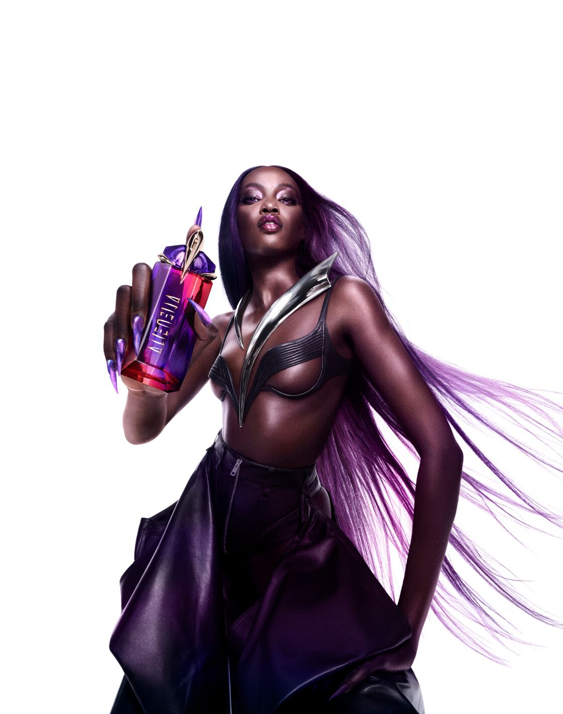 A model poses confidently, holding a vibrant perfume bottle, wearing a stylish outfit with dramatic hair flowing.